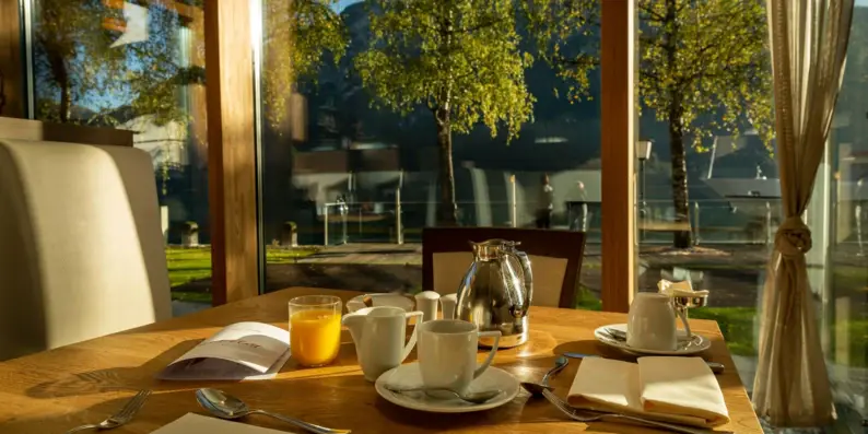Ein Frühstückstisch mit einer Teekanne und Tassen vor einer Glaswand. Ein Frühstückstisch mit einer Teekanne und Tassen vor einer Glaswand.