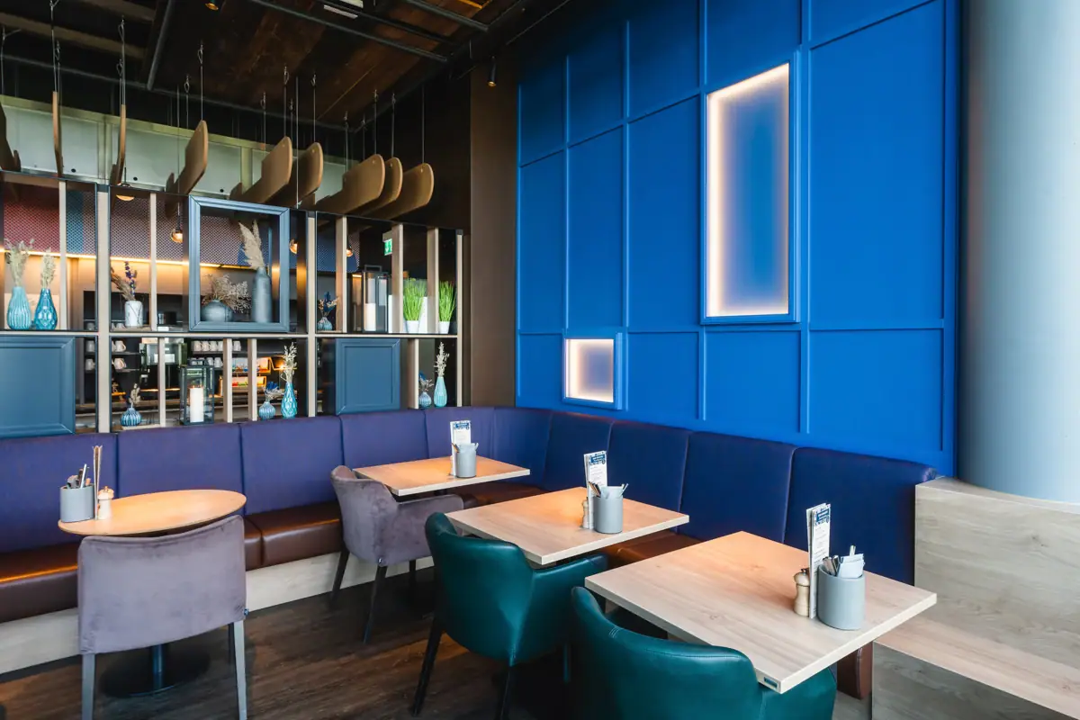 Restaurant im aja Warnemünde Blaue Sitzbank mit Tischen und Stühlen im Restaurant.