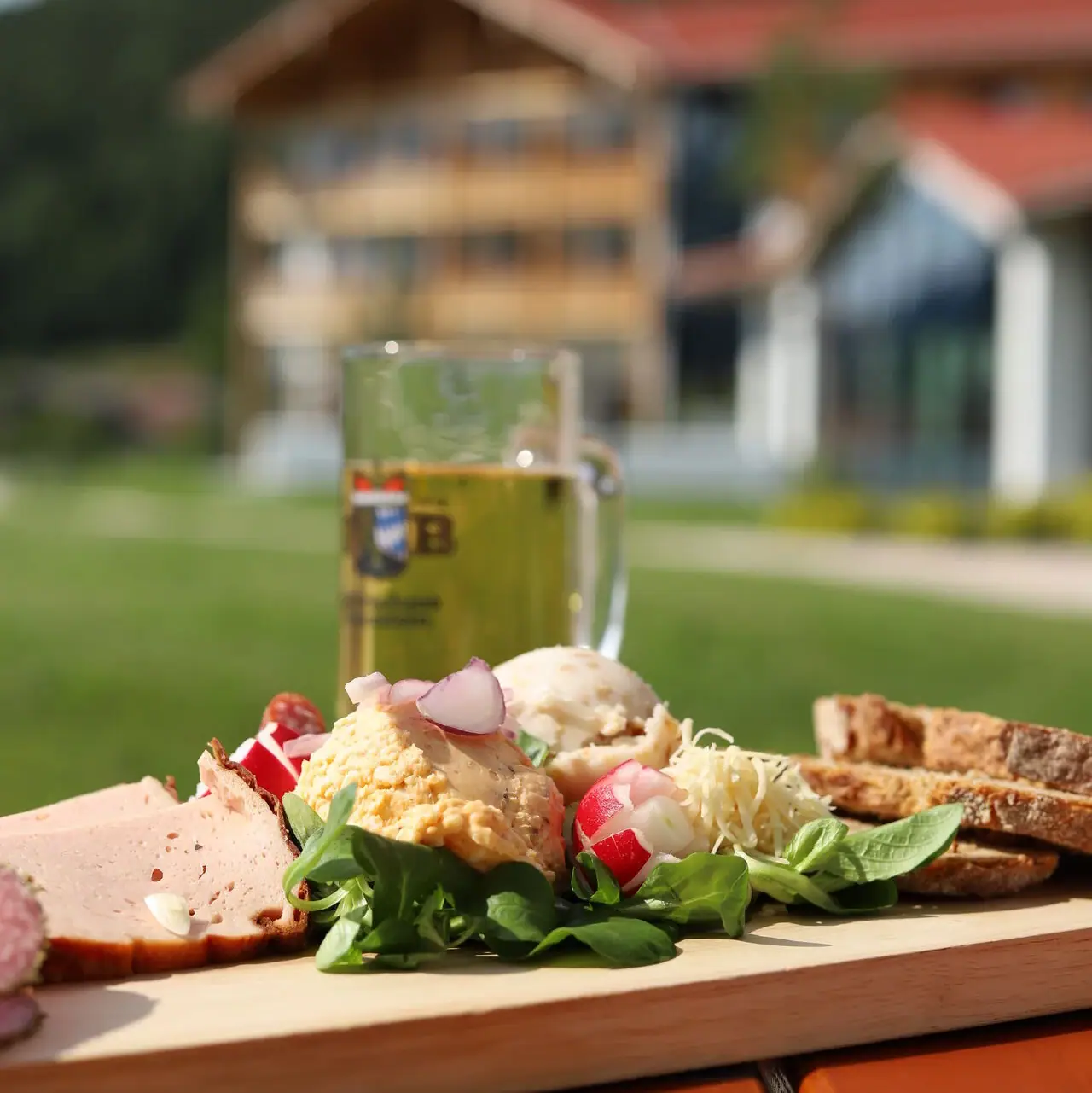 Brotzeit Ein Teller mit Essen und ein Glas Bier auf einem Holztisch im Freien.