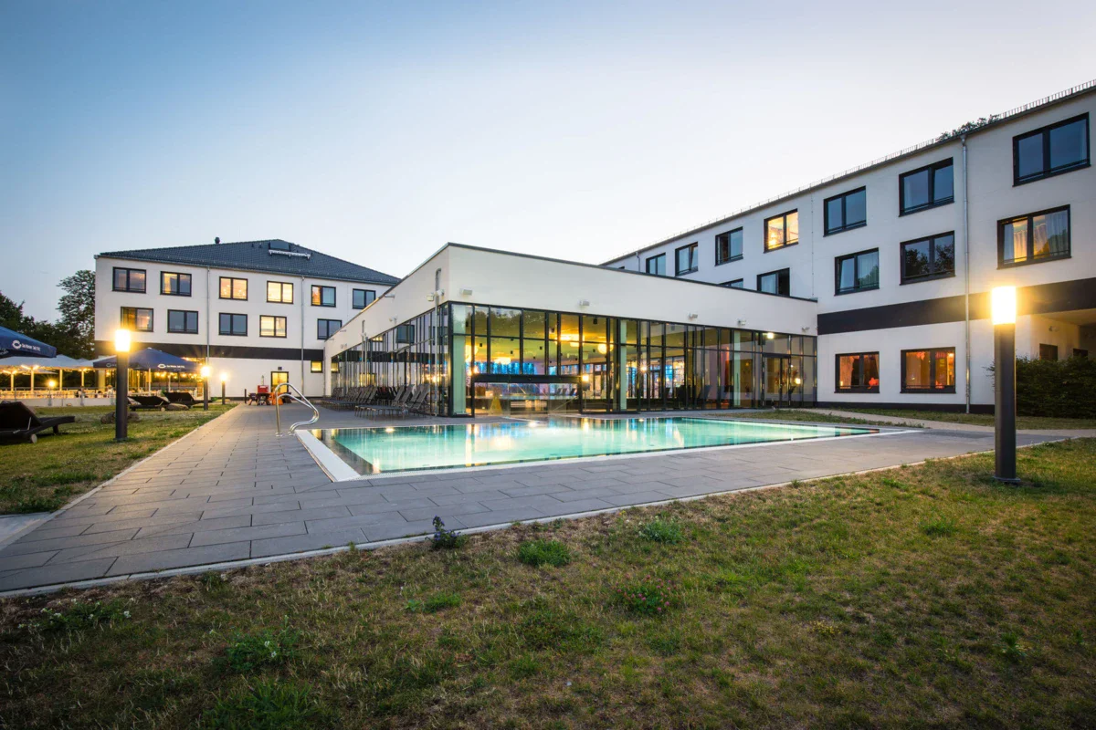 aja Bad Saarow Ein Hotelgebäude mit einem Swimmingpool und Rasen.