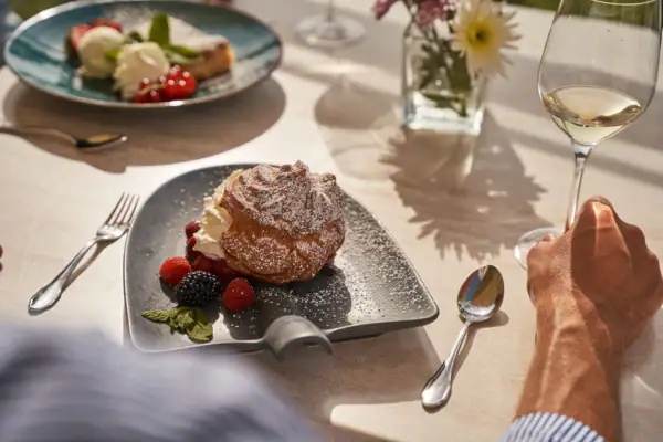 Café Nordstrand Ein Teller mit Dessert und Beeren neben einem Glas Wein.