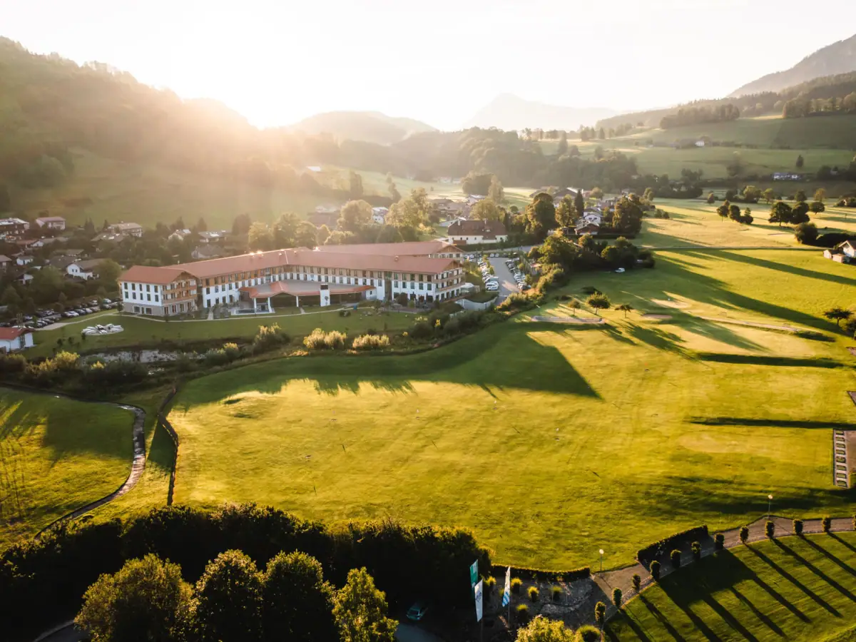 aja Ruhpolding Grünes Feld mit einem Gebäude und Bäumen im Hintergrund.