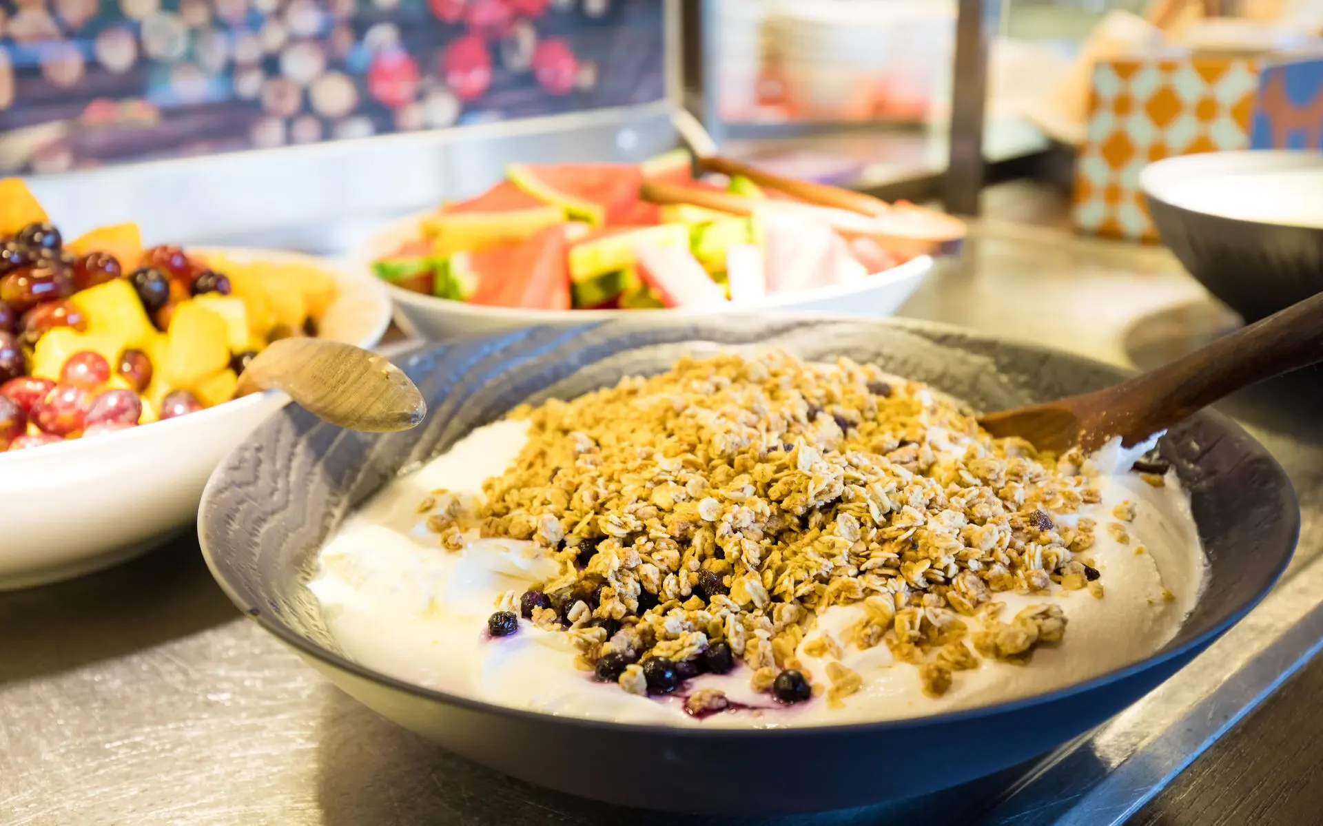 Frühstück im aja Warnemünde Mehrere Schalen, gefüllt mit Yogurt und Müsli, Früchten und Wassermelone stehen auf einem Buffetabschnitt.