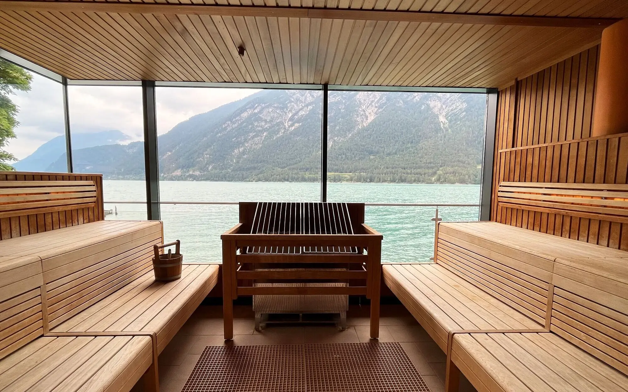 Sauna aja Fürstenhaus am Achensee Große Panoramasauna mit Blick auf Wasser und Berge, ausgestattet mit Holzbänken.