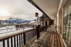 Balkon Ein Mann und eine Frau stehen auf einem Deck und blicken auf einen verschneiten Berg.