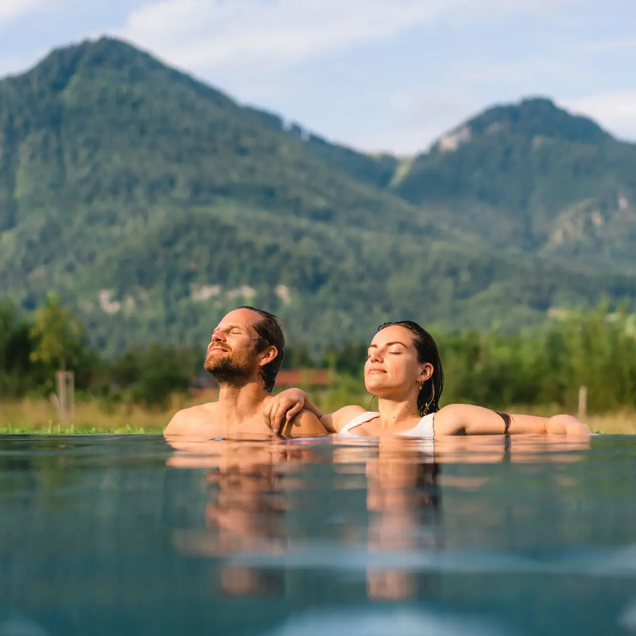 Day SPA in Ruhpolding Ein Mann und eine Frau im Pool mit Bergen im Hintergrund.
