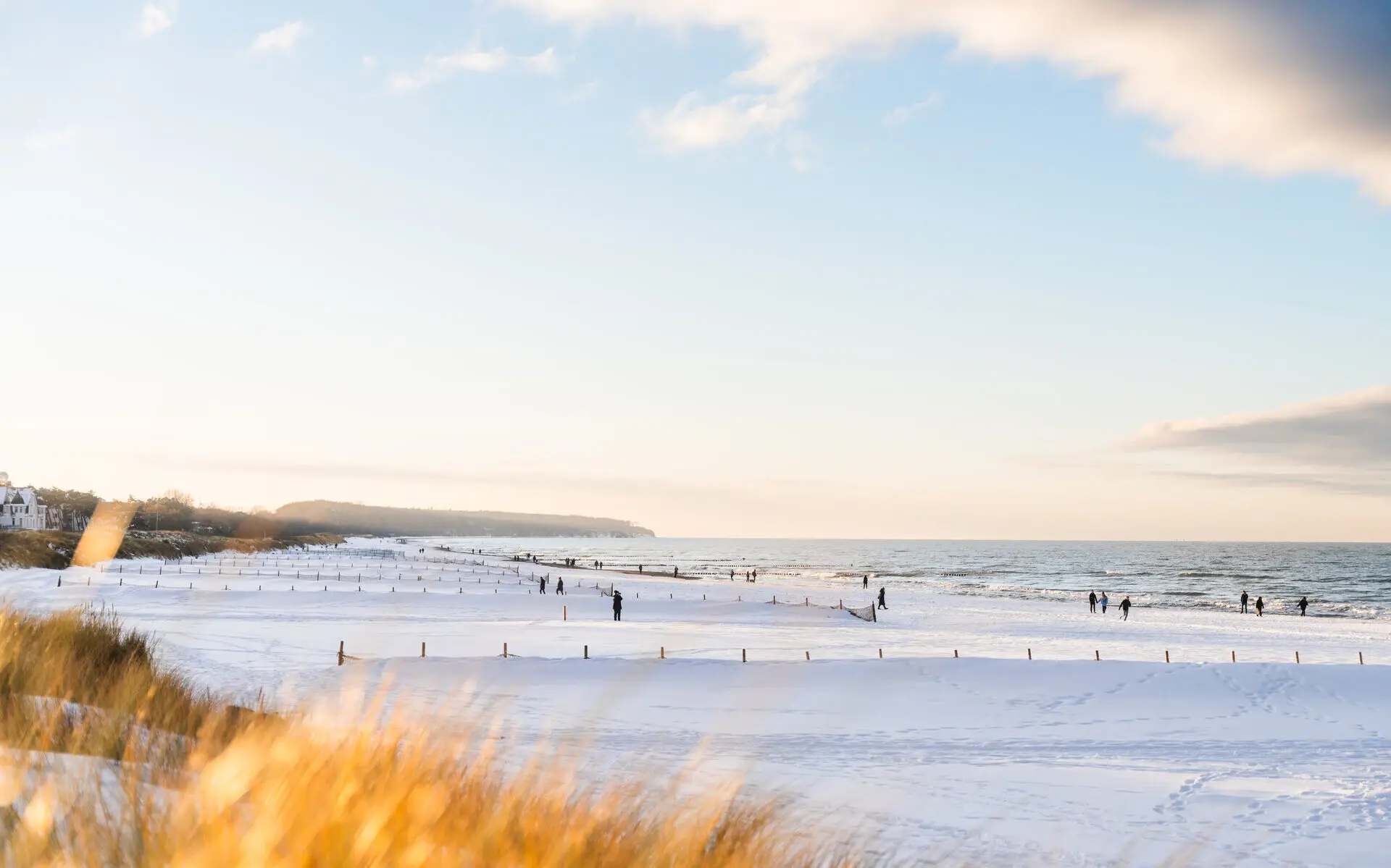 Winter in Warnemünde Strand bedeckt mit Schnee, Menschen und Bäume im Hintergrund.