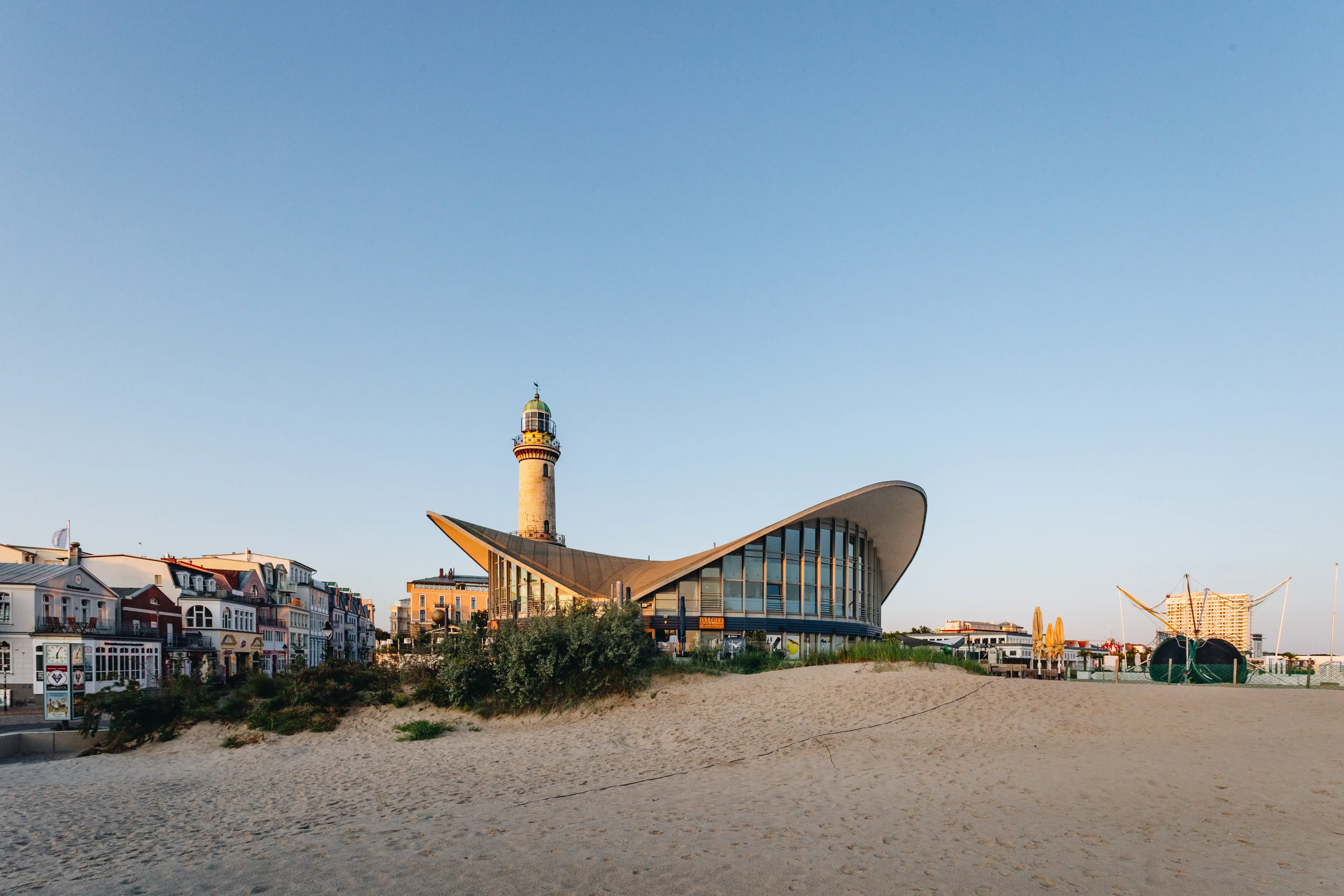 Ein Gebäude mit geschwungenem Dach und einem Leuchtturm im Hintergrund an einem kühlen sonnigen Tag.