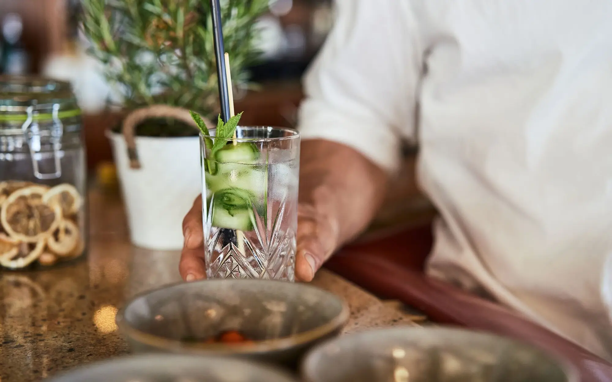 Cocktail Ein Mann hält ein Longdrinkglas auf einer Bartheke.