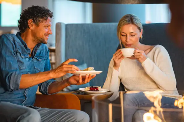 aja Bar Warnemünde Ein Mann und eine Frau sitzen am Kamin auf einer Couch und essen.