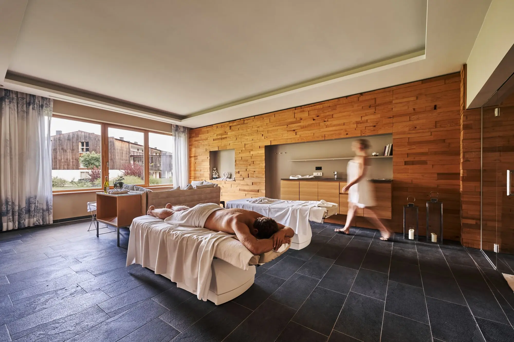 SPA Suite Werfenweng Mann liegt auf einer Massageliege in einem Raum, während eine Frau durch den Raum geht.