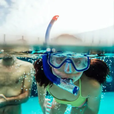Schwimmkurse Ein Mädchen in Badeanzug und Schwimmbrille unter Wasser.
