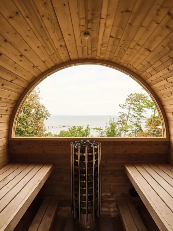 Fasssauna Eine Fasssauna aus Holz mit rundem Fenster, das auf das Wasser blickt.