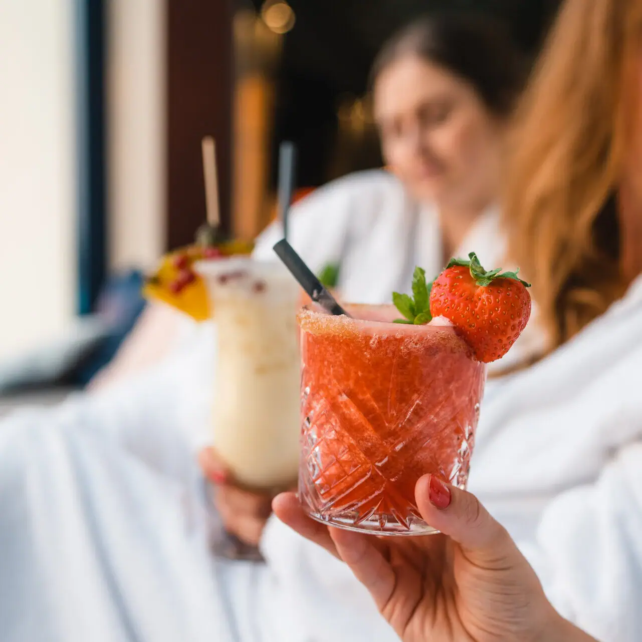 Cocktails Hand hält zwei Getränke, eines mit Erdbeergarnitur.