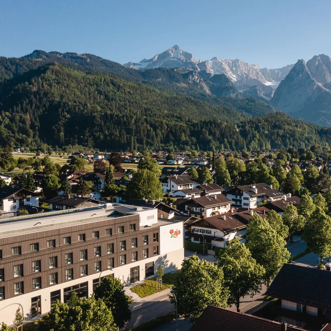 aja Garmisch-Partenkirchen Das aja Garmisch-Partenkirchen mit Bäumen und Bergen im Hintergrund.