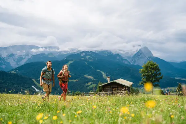 Wandern in Garmisch-Partenkirchen Ein Mann und eine Frau gehen in einem Feld mit Bergen im Hintergrund.