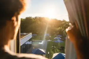 Ausblick Zimmer Bad Saarow Eine Person betrachtet einen Pool mit Sonnenschirmen und Bäumen.