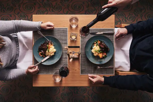 Restaurant Flora Eine Person hält eine Weinflasche und isst Essen.