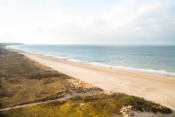 Strand Warnemünde Strand mit Gras und Sand unter bewölktem Himmel.