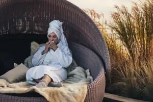 SPA Eine Frau sitzt mit Bademante in einem Korbstuhl und trinkt aus einer Tasse.