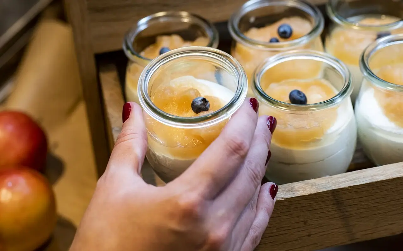 Dessert im aja Grömitz Eine Frauenhand mit roten Fingernägeln nimmt ein Nachtischglas von einem Tablett mit Nachtisch.