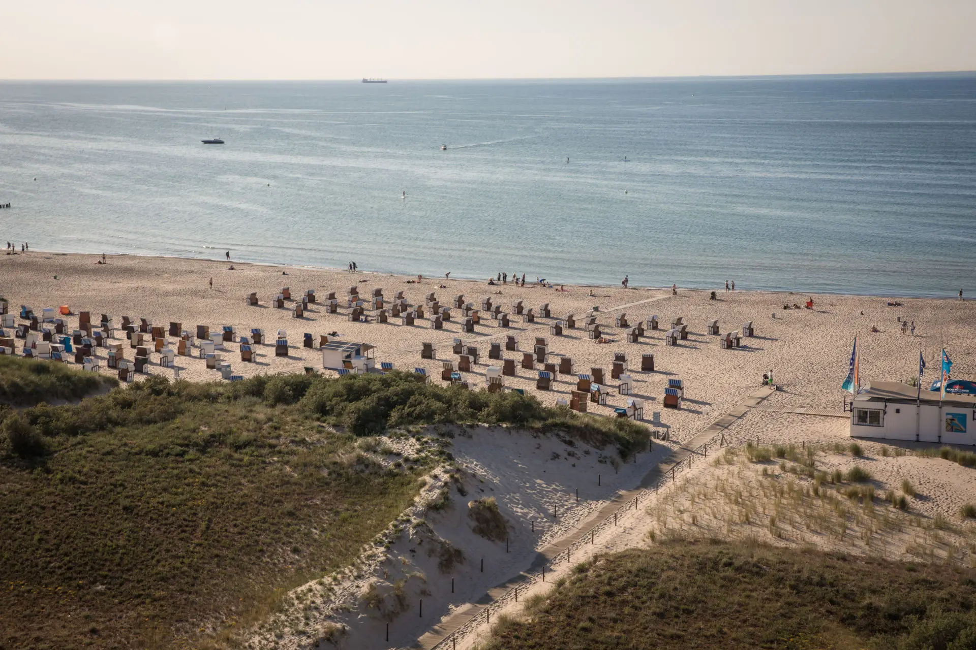Eine Luftaufnahme eines Strandabschnitts mit vielen aufgereihten Strandkörben und ruhigem Wasser an einem Frühlingstag.
