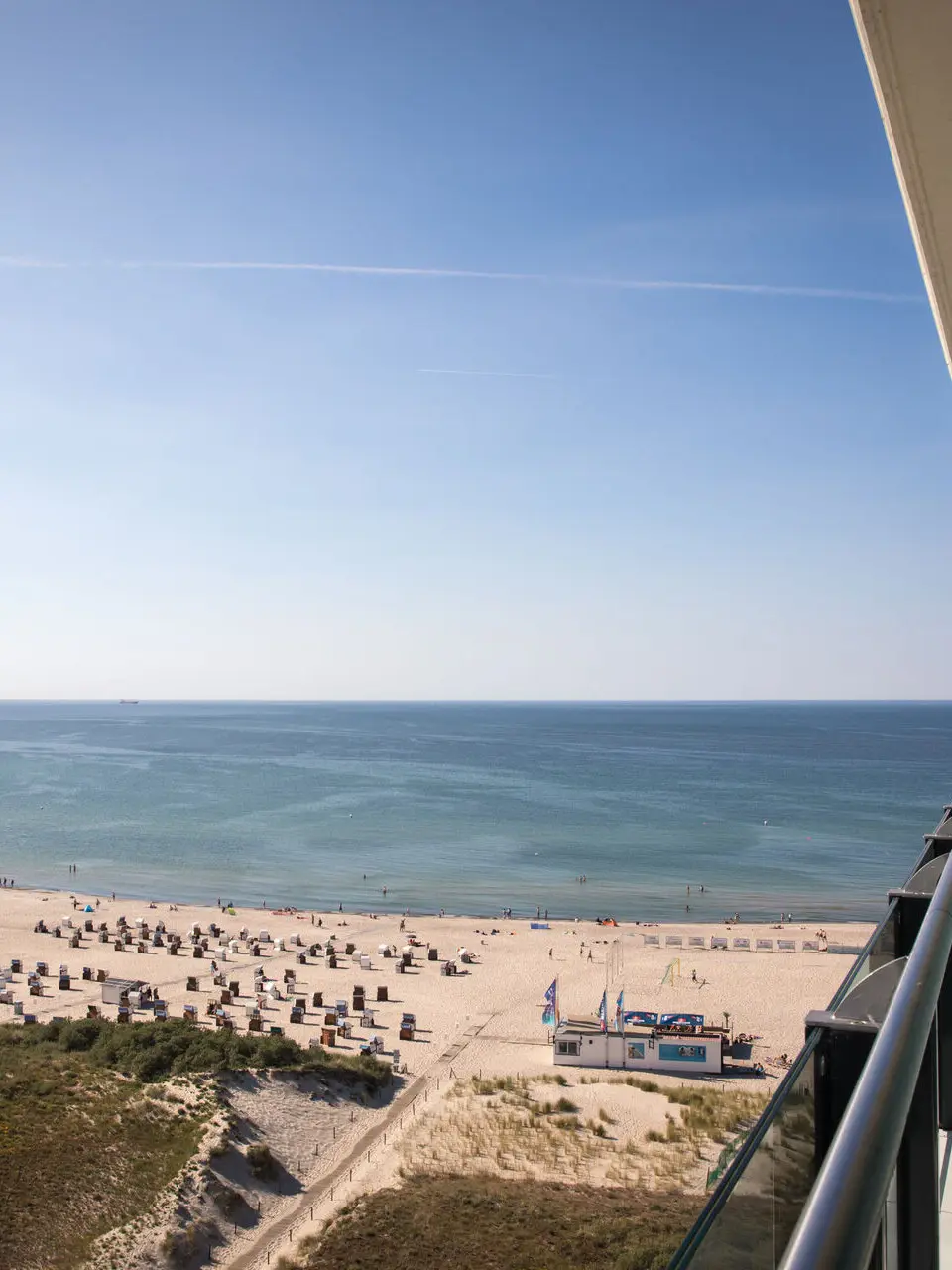 Ein Balkonausblick auf die sonnige Küste von Warnemünde mit Strand und blauem Meer.