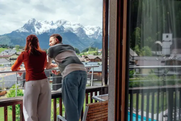 Zimmer mit Balkon Ein Mann und eine Frau stehen auf einem Balkon und blicken auf Berge.