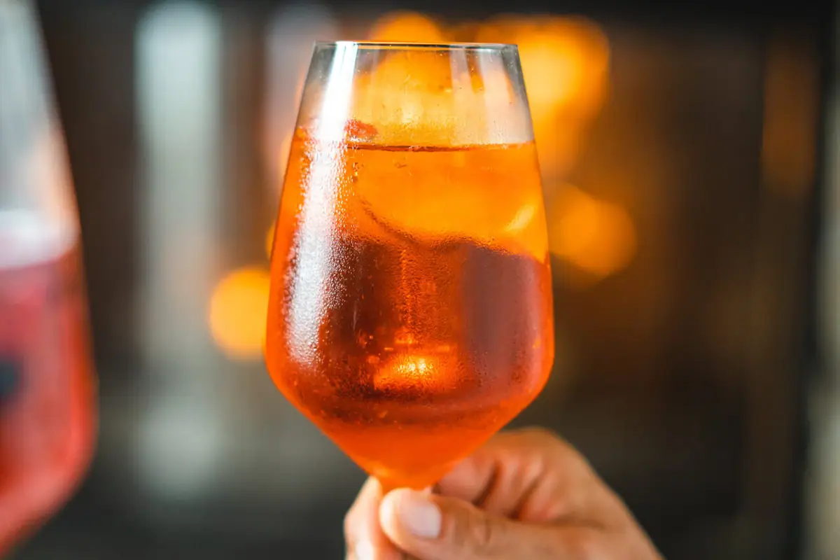 Aperol Eine Hand hält ein Glas mit orangefarbener Flüssigkeit.