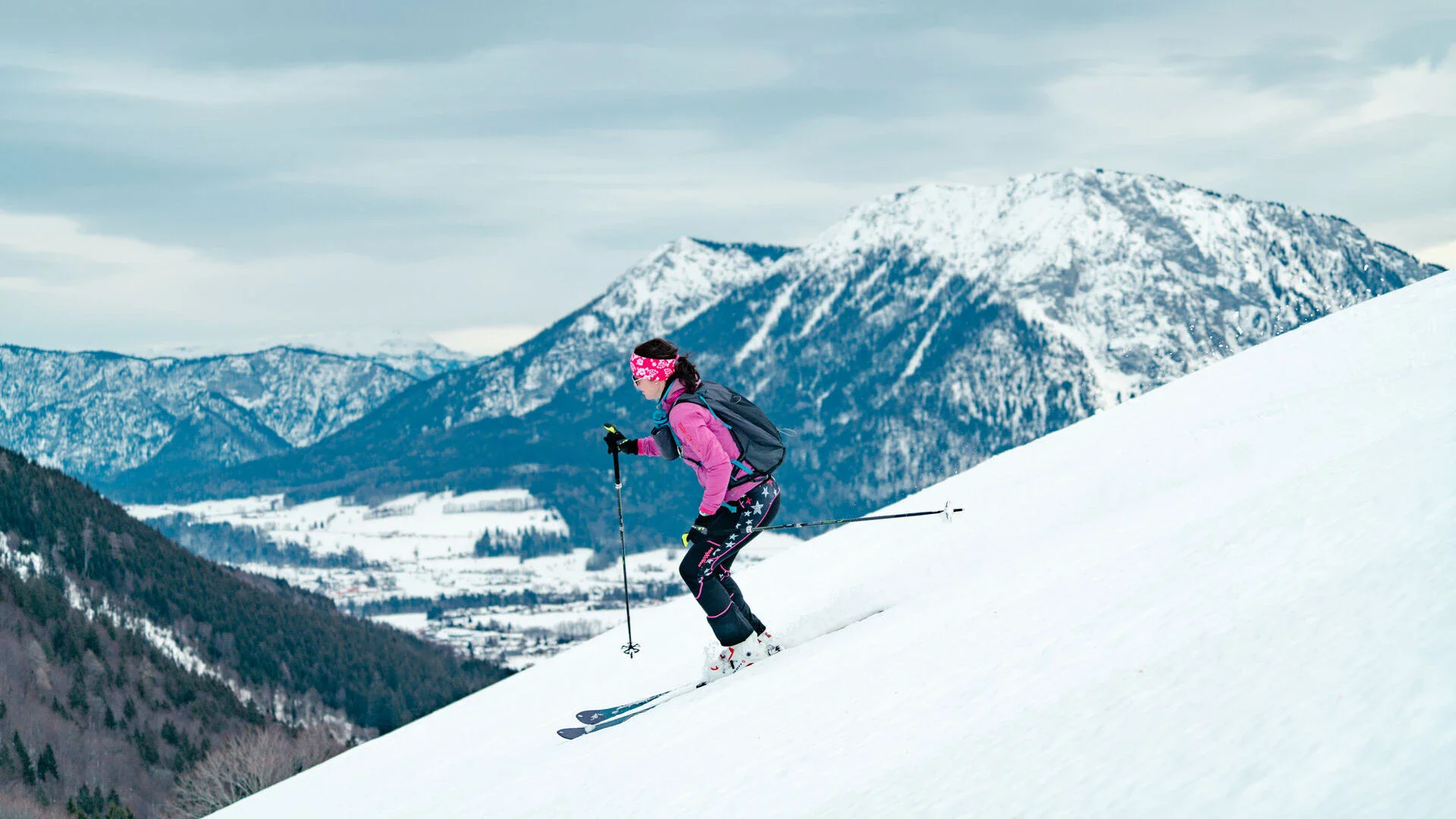 Eine Frau in schwarzer und pinken Skikleidung fährt schneebedeckte Berge hinunter.