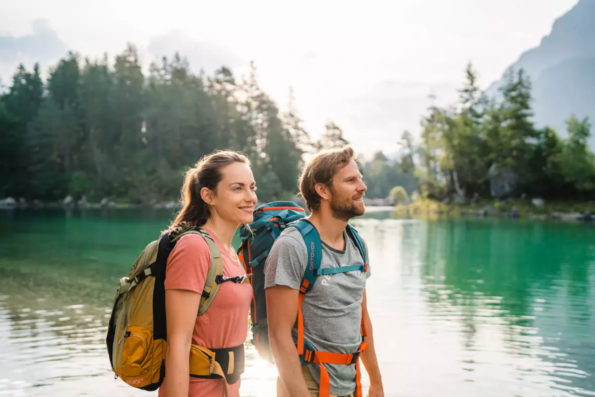 Eibsee wandern Ein Mann und eine Frau mit Rucksäcken stehen vor einem Gewässer.