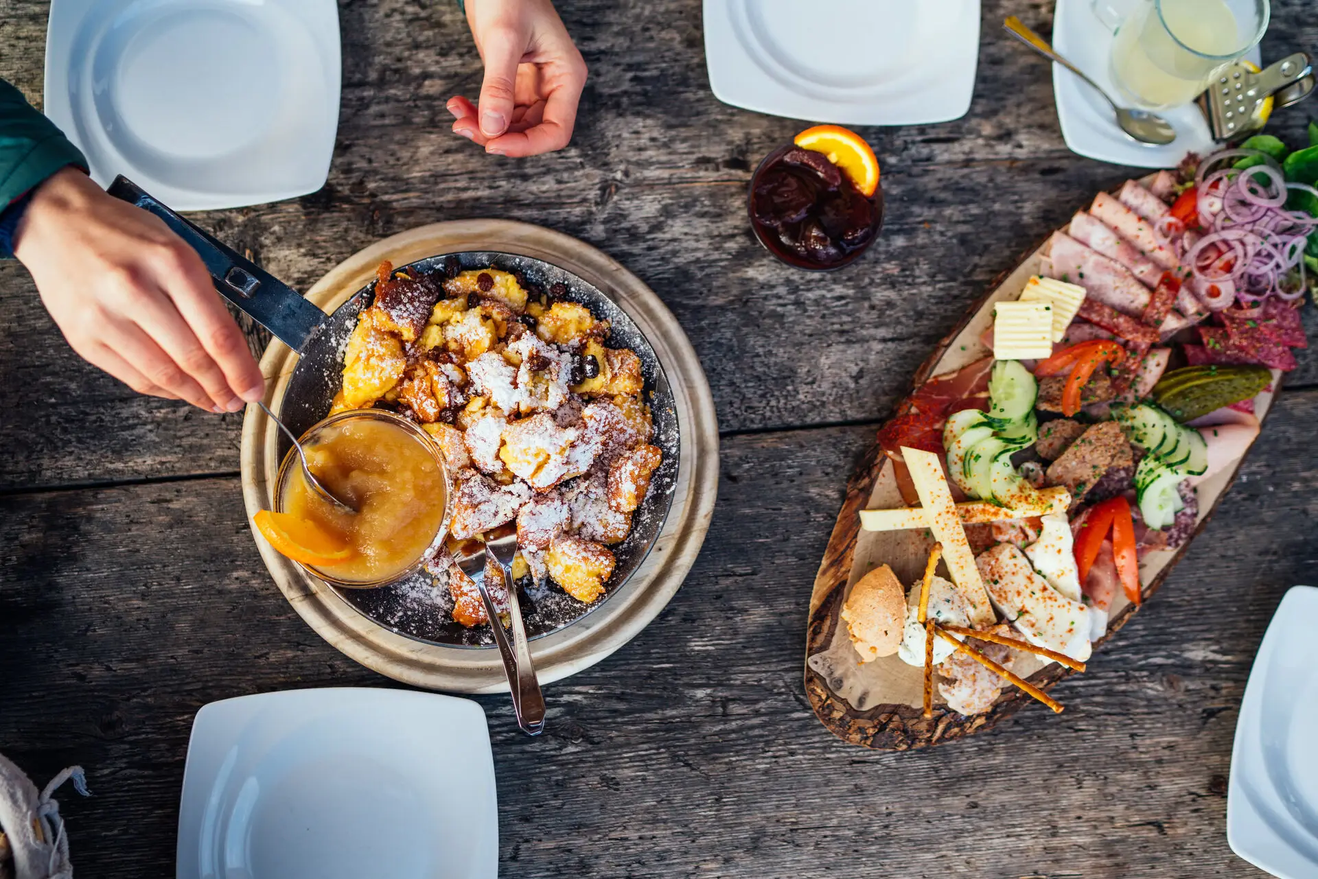 Essen im aja Garmisch-Partenkirchen Auf einem Holztisch steht eine Pfanne Kaiserschmarren und ein Brett mit Aufschnitt.