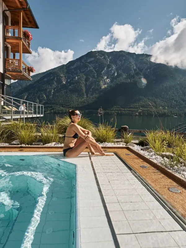 Eine Frau sitzt an einem Pool mit einem Berg im Hintergrund.