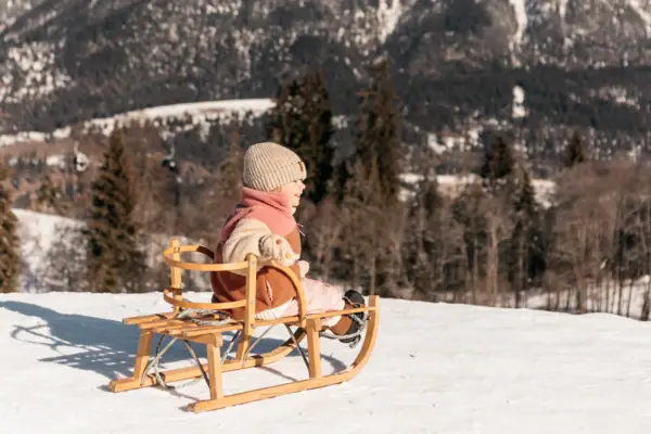 Schlittenfahrt Ein Kind sitzt auf einem Schlitten im Schnee.