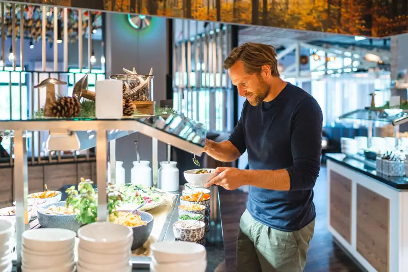 Ein Mann steht an einem Salatbuffet und stellt sich sein Essen zusammen.