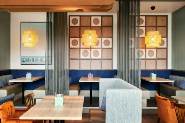 Bar im aja Warnemünde Ein Raum mit Tischen und Stühlen und einzelnen Kojen, abgetrennten Bereichen.