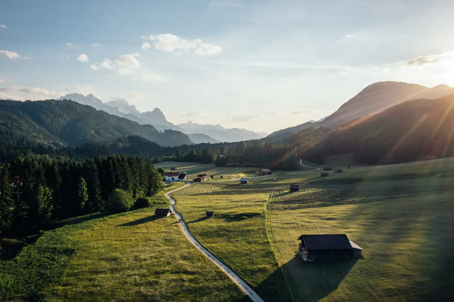 Garmisch-Partenkirchen Straße, die zu einem grünen Feld mit Gebäuden und Bergen im Hintergrund führt