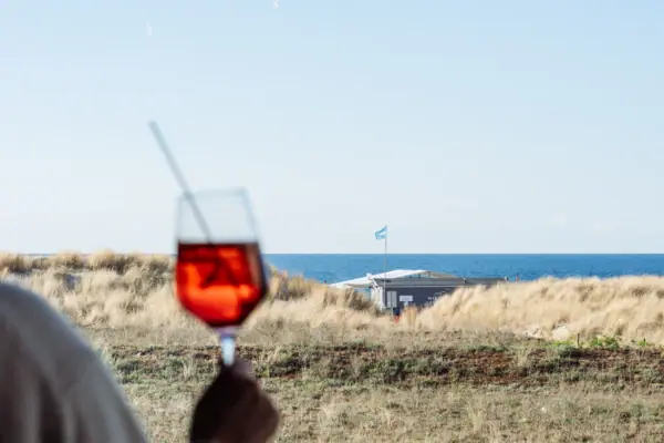 Drink mit Aussicht Eine Person hält ein Glas mit roter Flüssigkeit und einem Strohhalm vor dem Ozean.