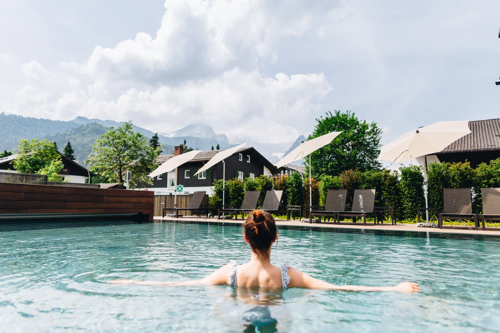 Eine Frau schwimmt in einem blauen Außenpool mit Blick auf die Berge und umliegende Häuser.