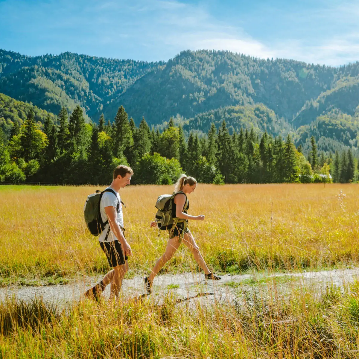 Wandern in Ruhpolding Ein Mann und eine Frau wandern auf einem Pfad in einem Feld mit Bergen im Hintergrund.