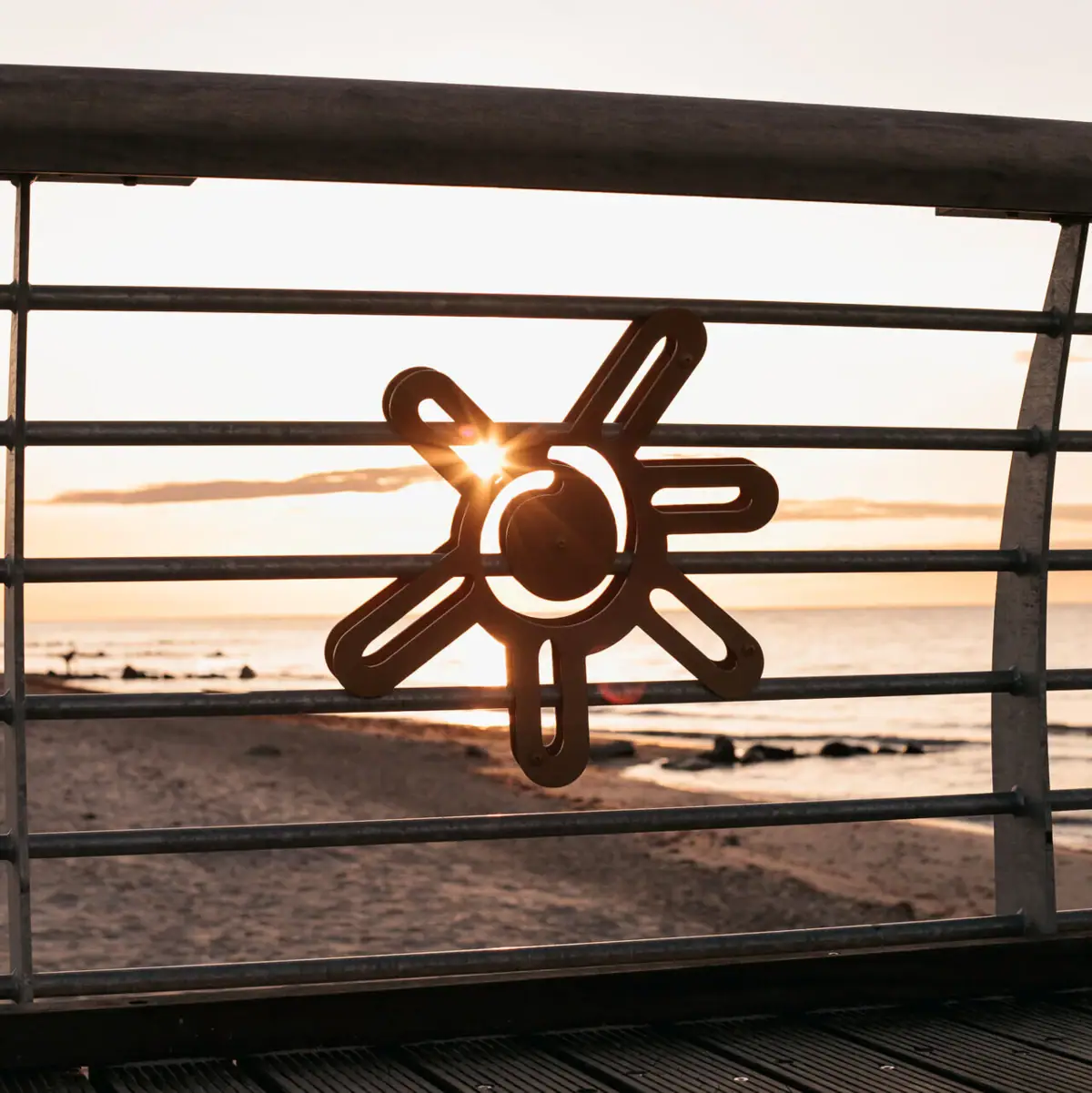 Sonne auf der Seebrücke Metallgeländer mit Sonnensymbol darauf.