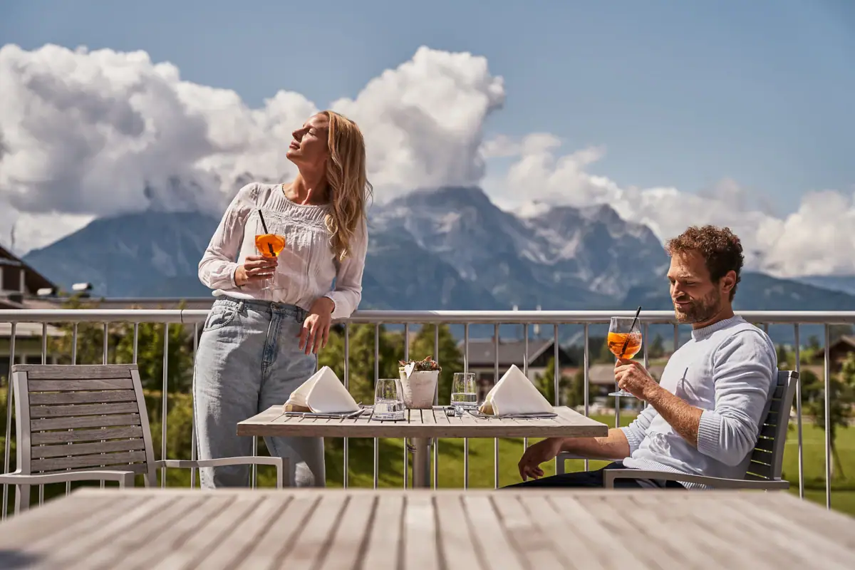 Ein Mann und eine Frau trinken aus einem Glas auf einer Terrasse.