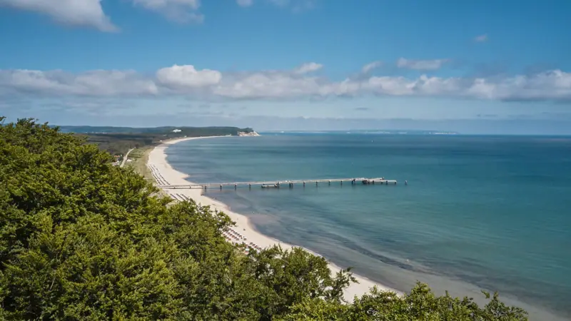Küste von Rügen Strand mit einem Pier und Bäumen im Vordergrund.