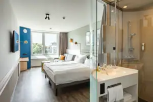 Zimmer im aja Warnemünde Ein Zimmer mit einem Doppelbett und einem offenen Bad mit einer Dusche.