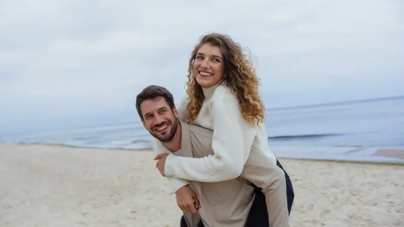 Strandurlaub Ein Mann trägt eine Frau auf dem Rücken am Strand.