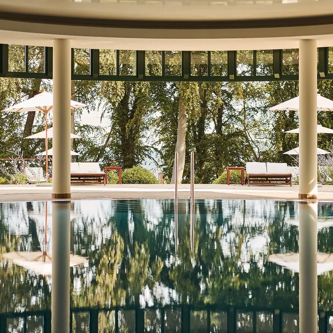 Innenpool Ein Pool mit Sonnenschirmen und Stühlen im Hintergrund.