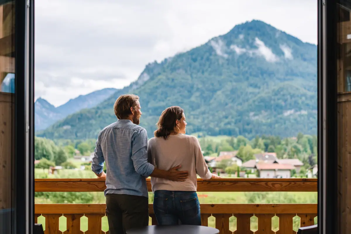 Ein Mann und eine Frau stehen auf einem Balkon mit Blick auf ein Gebirge.
