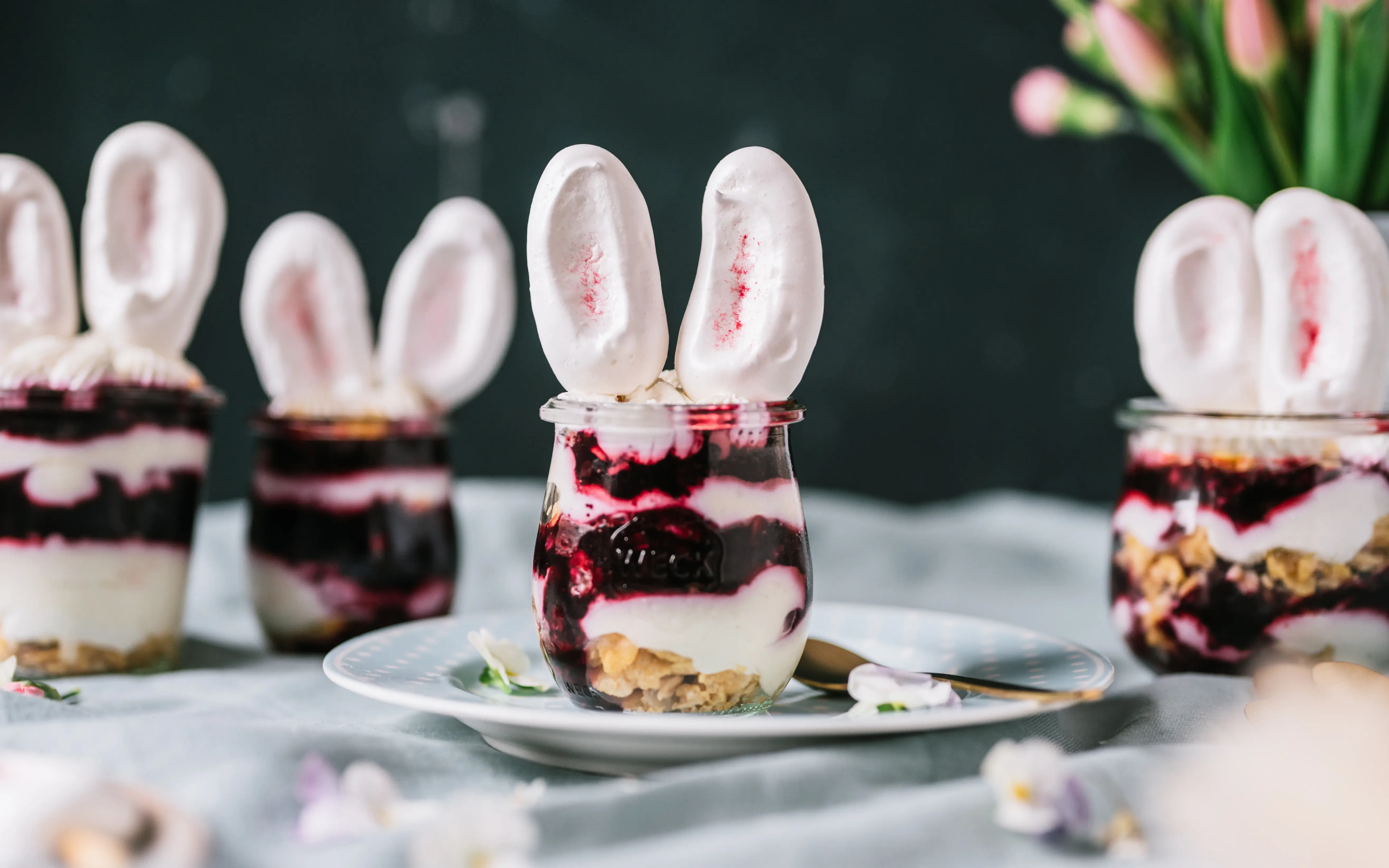 Ein kreatives Dessert in Gläsern, geschichtet mit Joghurt, Beeren und Meringue-Ohren, passend dekoriert für Ostern.