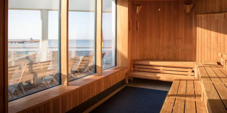 Ausblick aus einer hölzernen Sauna hinaus durch drei breite Panoramafenster auf den Sandstrand und das Wasser der Ostsee. Ausblick aus einer hölzernen Sauna hinaus durch drei breite Panoramafenster auf den Sandstrand und das Wasser der Ostsee.