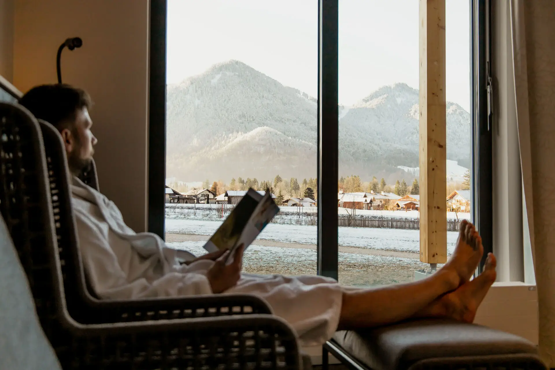 Ruheraum aja Ruhpolding Ein Mann entspannt in einem Ruheraum in einem Sessel, List ein Buch und schaut aus dem Fenster.